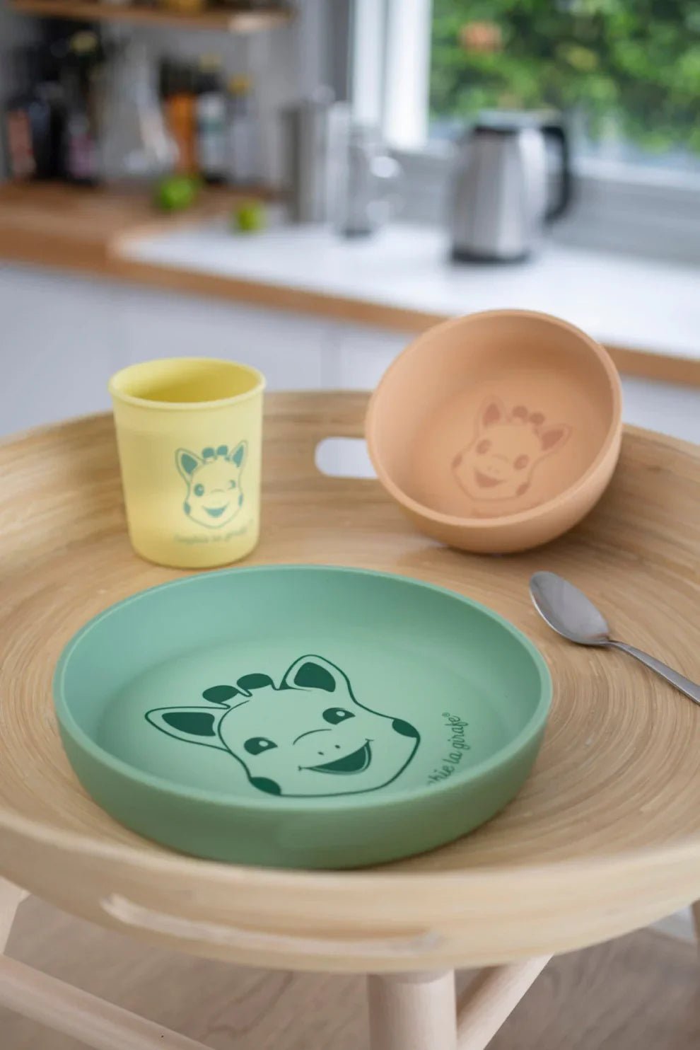 Kids silicone meal set on table: green plate, tan bowl, yellow cup, small spoon