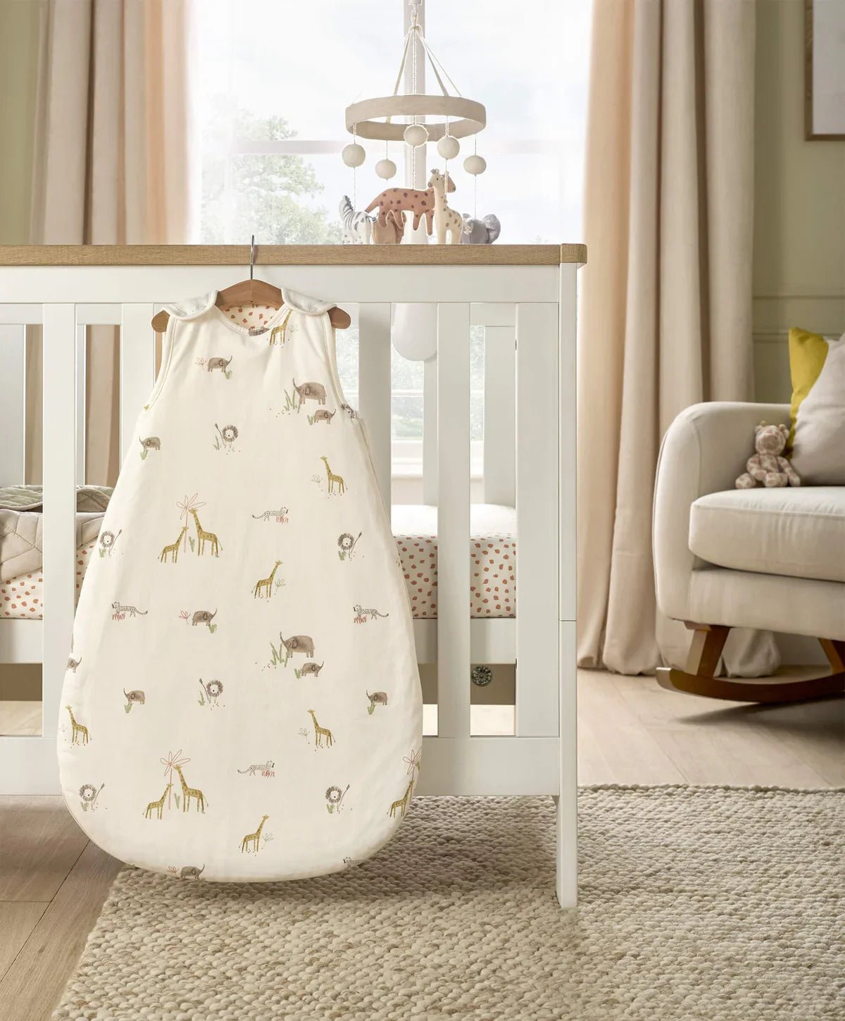 Baby sleep sack with off-white jungle animal print, hanging on crib