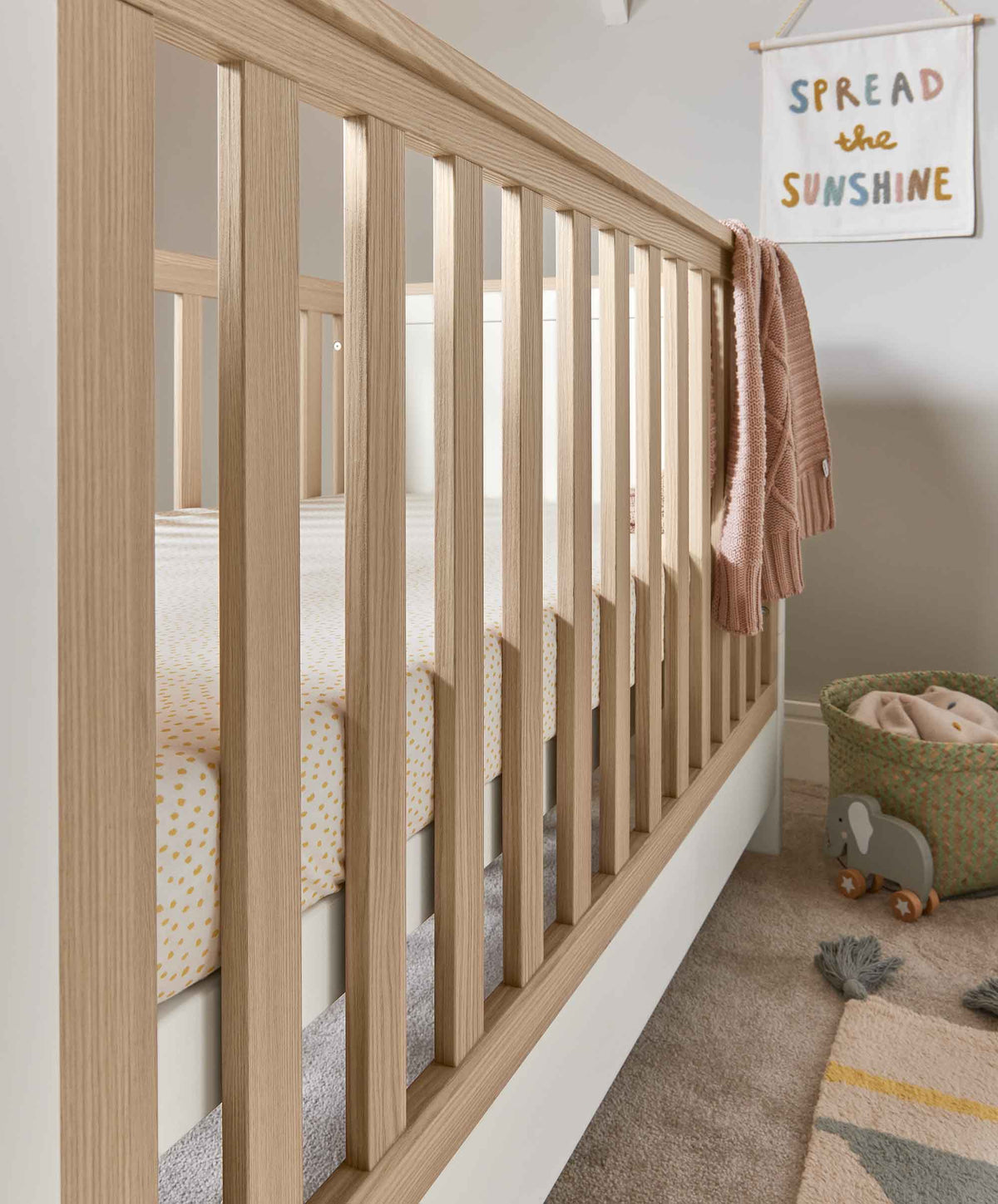 Wood and white cot end panel with vertical slats and knitted blanket on the rail