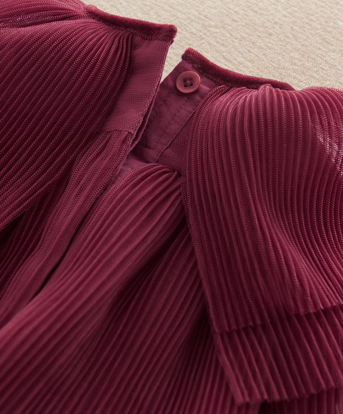 Burgundy button-up neckline with pleated cape detail