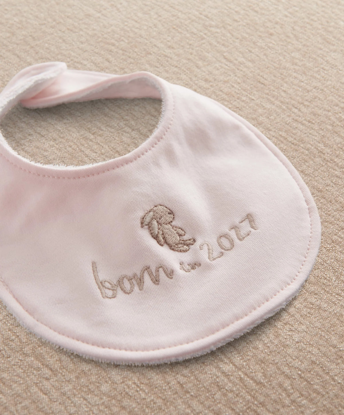 Pink baby bib with rounded neck, embroidered bear and 'born in 2027' text