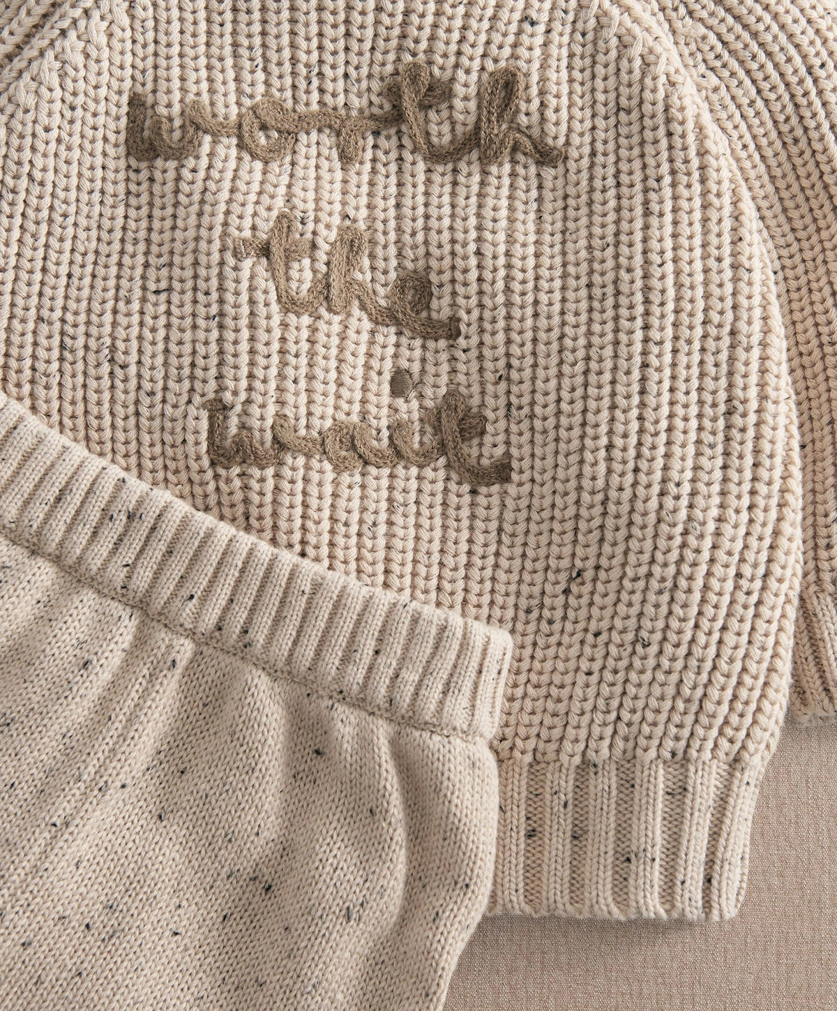 Close-up of cream knit sweater with embroidered snails and ribbed cuffs