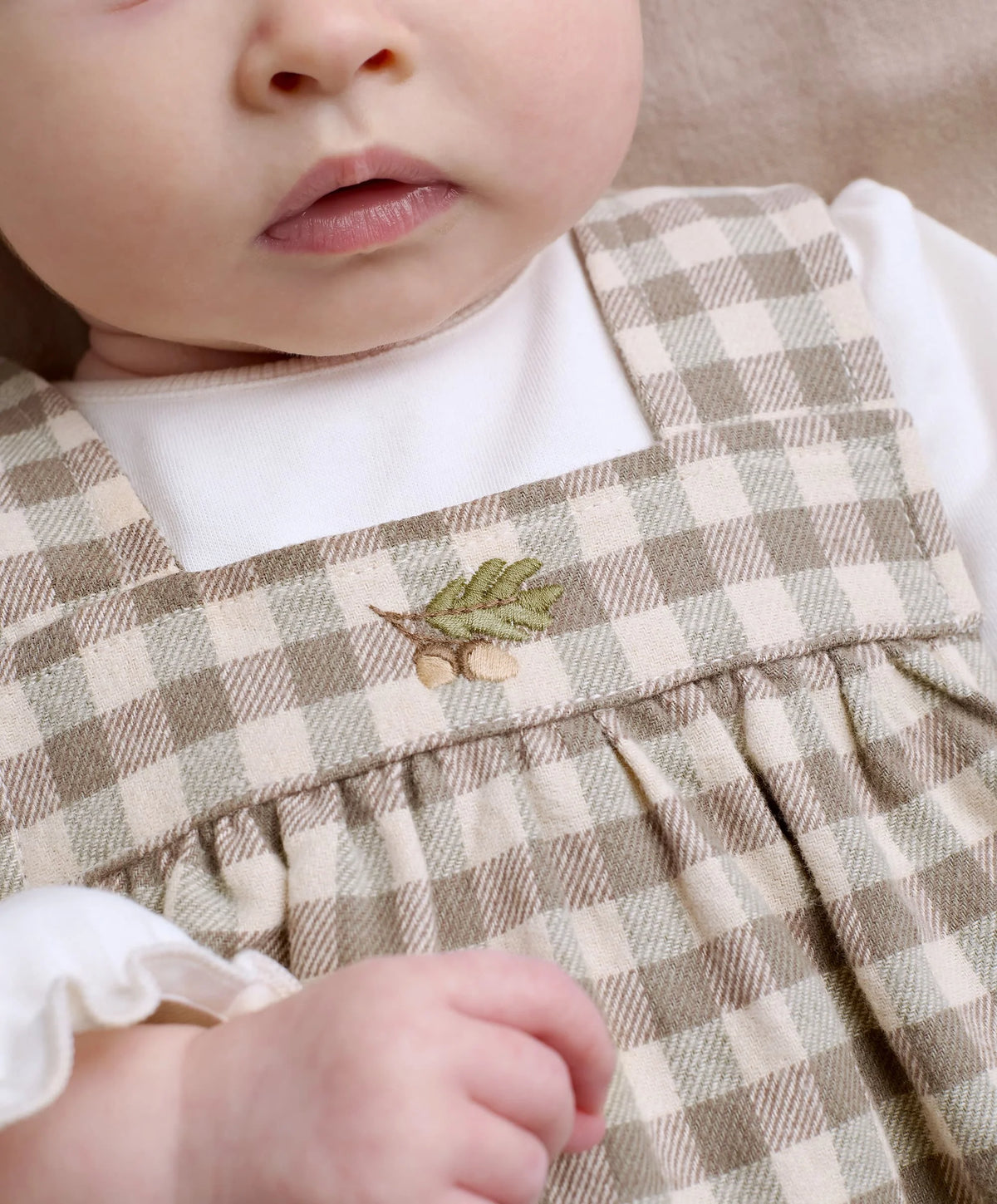 Baby gingham pinafore dress over white bodysuit, green leaf patch on gathered ruffle front