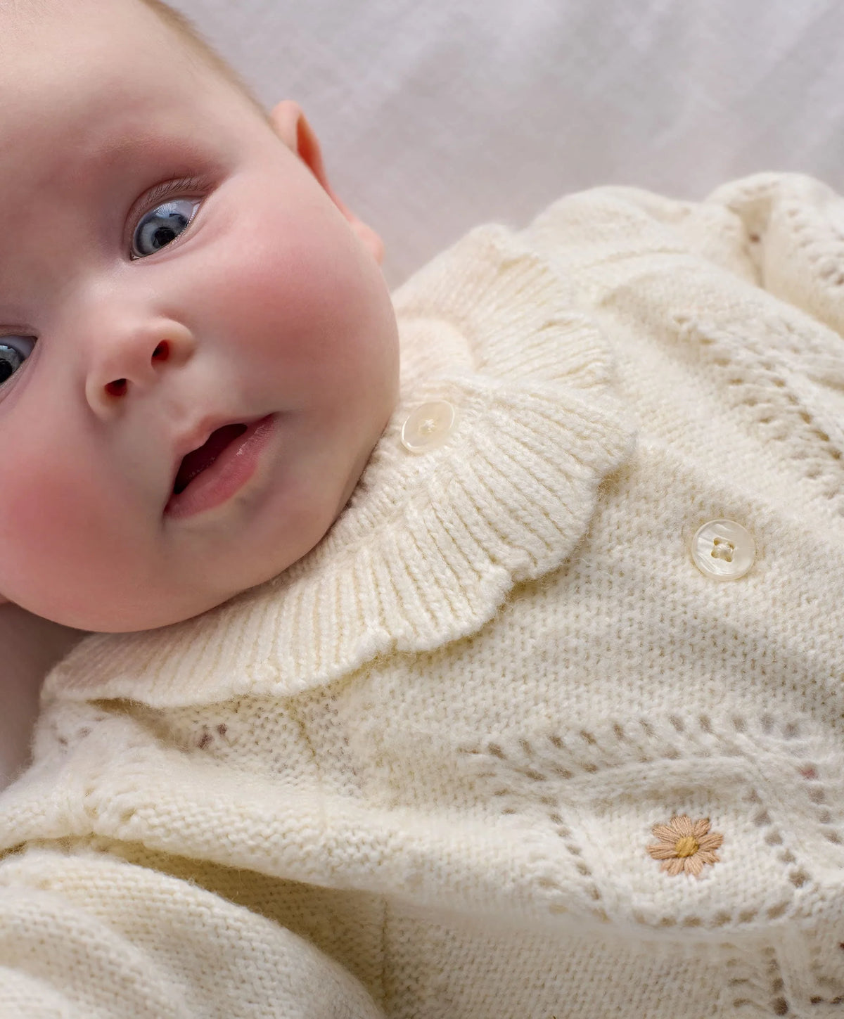 Cream knit cardigan close-up with textured stitch, floral embroidery, and button placket.