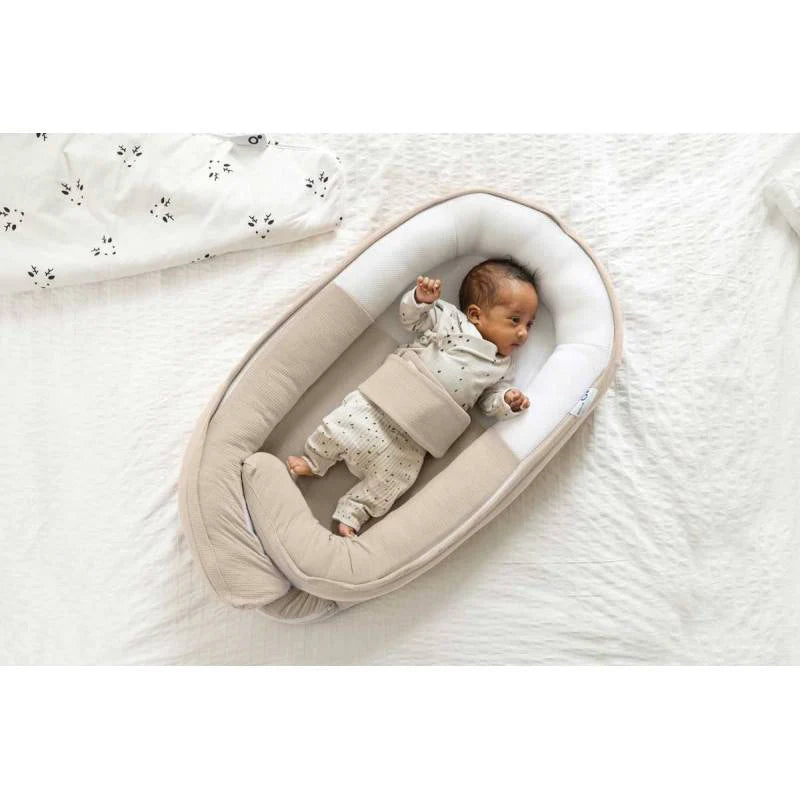 Sand beige baby cocoon nest on white bedding, curved head support