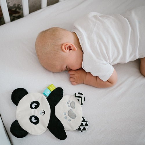 Flat cuddly panda plush toy beside a sleeping baby, white face and black ears