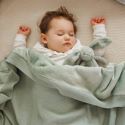 Green cotton flannel-lined blanket wrapped around a sleeping baby