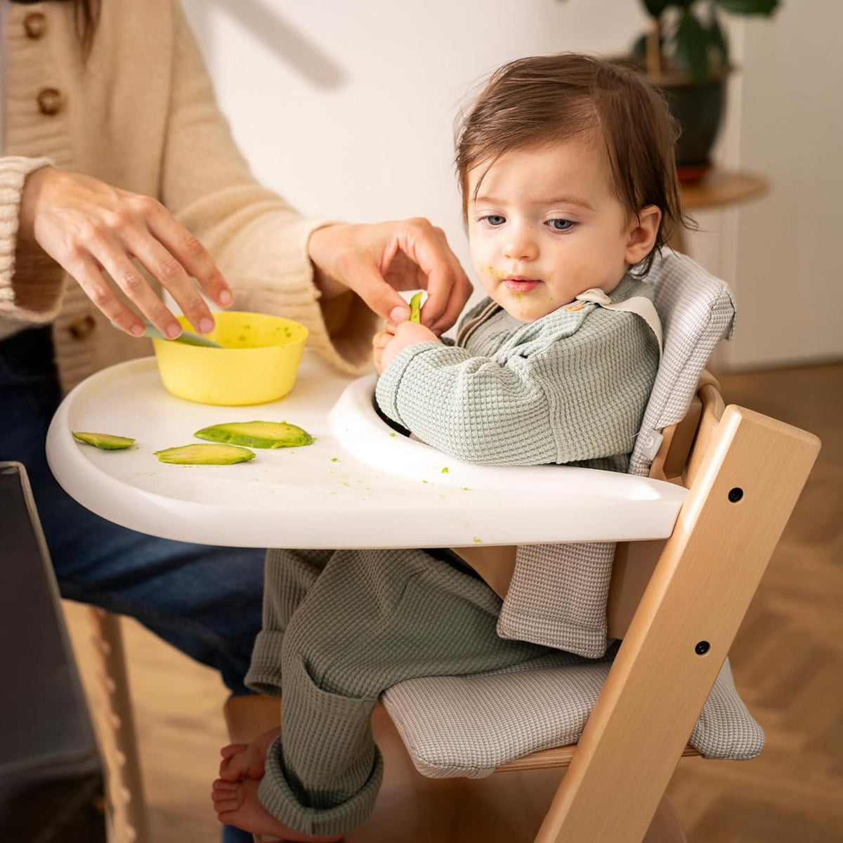 White high chair tray with raised edges, used during a toddler feeding moment