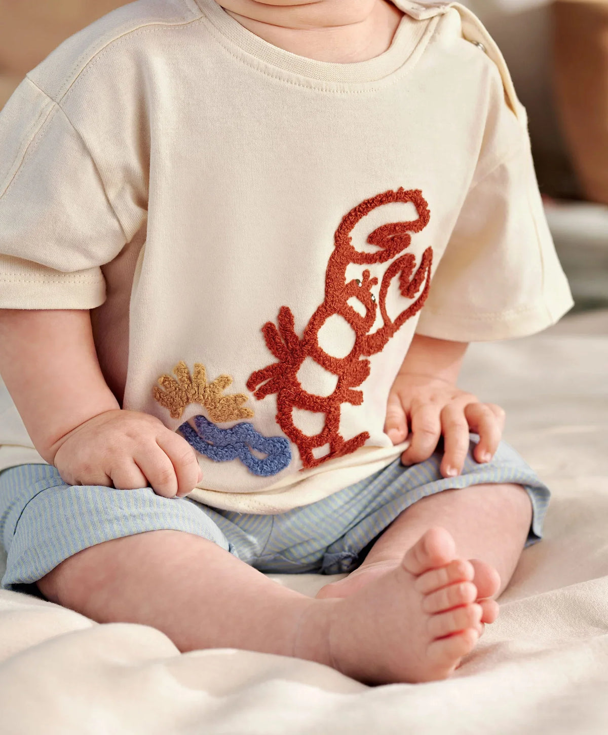 Cream t-shirt with red lobster and blue sea detail, paired with light blue shorts