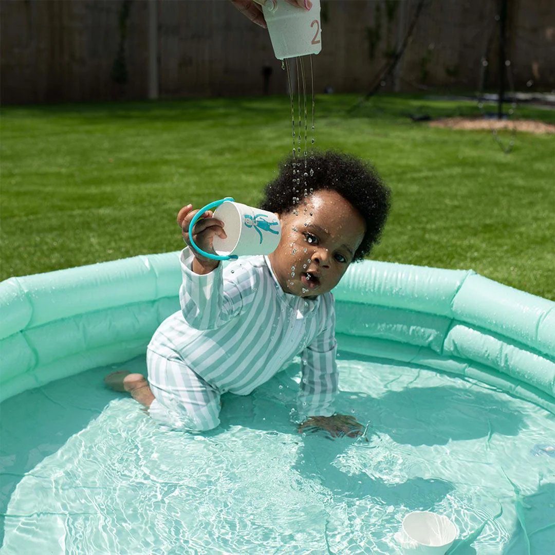 Child pouring water from a bath bucket into an outdoor inflatable pool