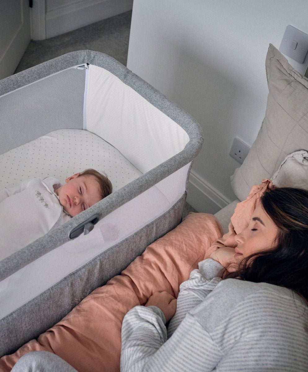 Grey bedside crib with padded rails and white inner base, baby inside