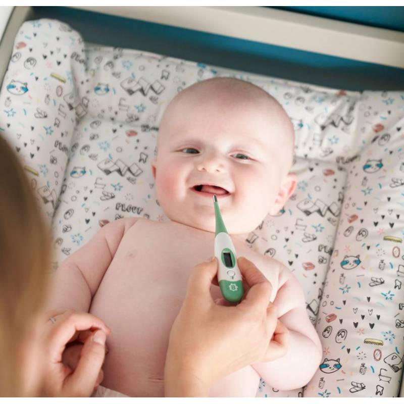 Green digital thermometer near a smiling baby held in a caregiver’s hand