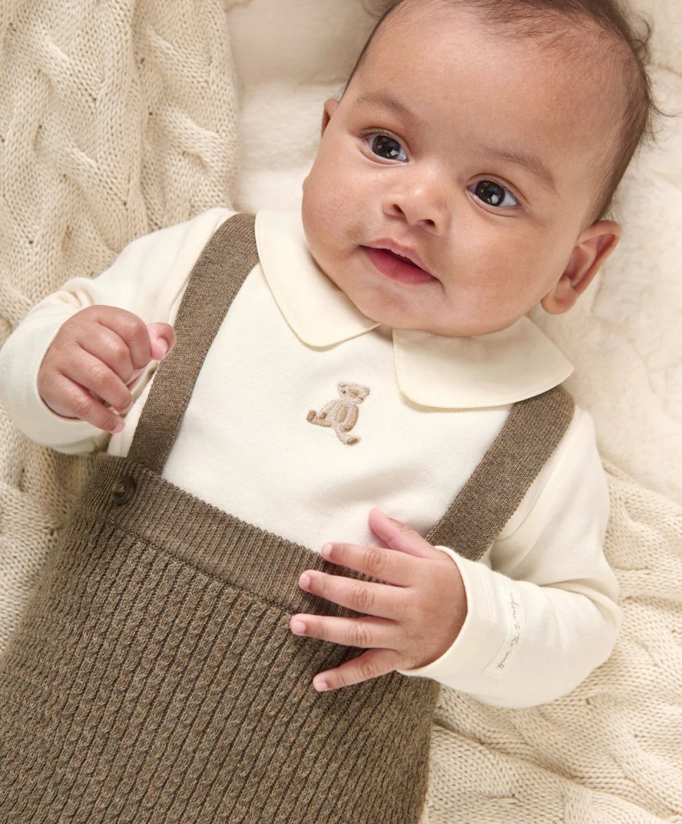 Cream teddy bodysuit with long sleeves and brown knitted dungarees on a baby