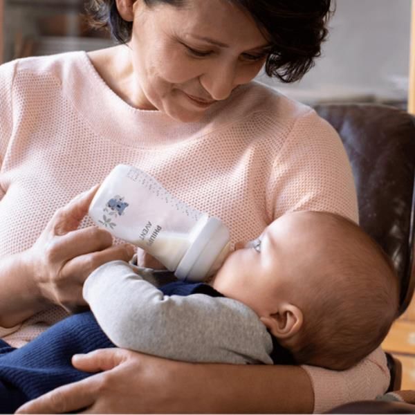 Baby feeding bottle with blue animal and leaf print, held during feeding