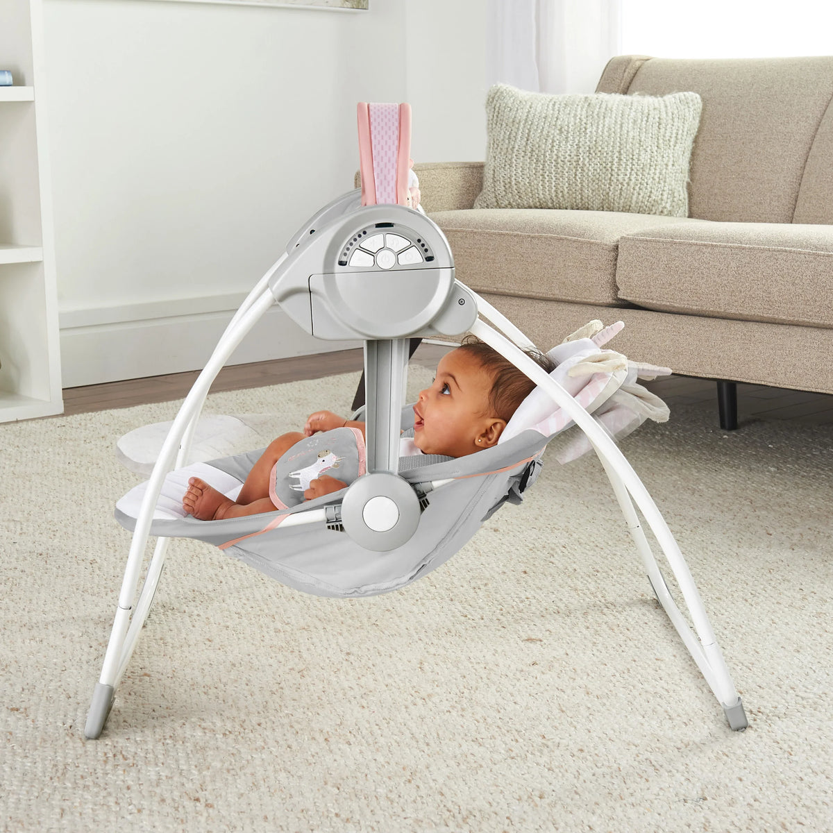 Portable baby swing with gray seat and white frame, baby sitting inside with toys