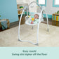White baby swing with hanging toys and padded seat, baby seated upright.