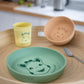Kids silicone meal set on table: green plate, tan bowl, yellow cup, small spoon