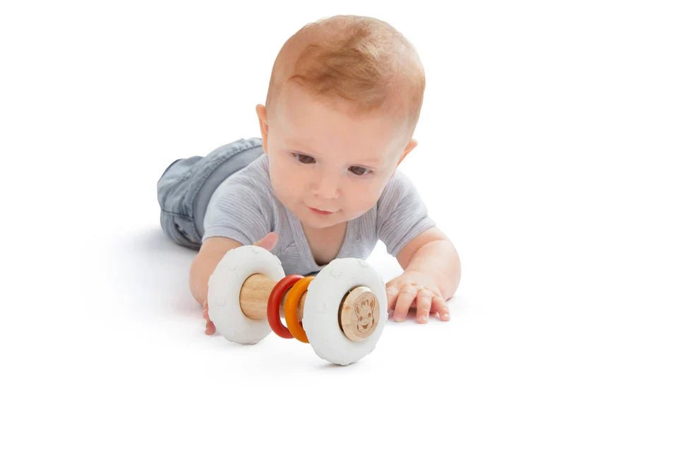 Totem rattle with white plush ends and colorful rings, held in a baby’s hands