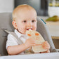 Baby holding a light-colored feeding pouch with a cat face