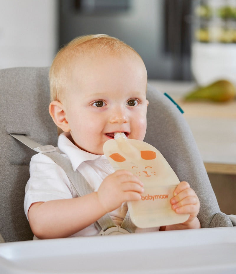 Baby holding a light-colored feeding pouch with a cat face