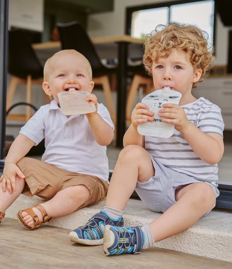 Two babies holding light-colored feeding pouches with cat faces