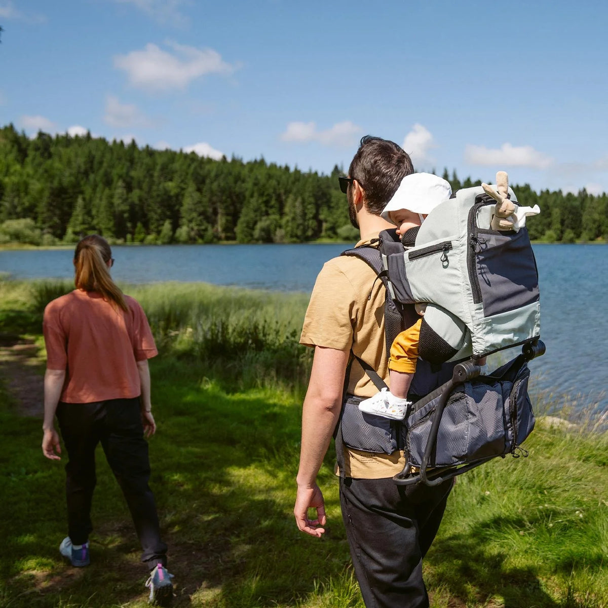 Green and dark baby hiking carrier worn from back with child seat and leg support.