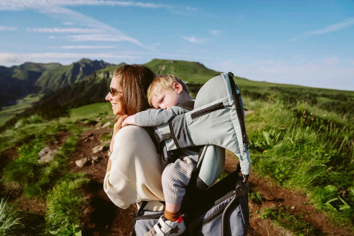 Baby hiking carrier with light-green canopy and padded shoulder straps holding child.