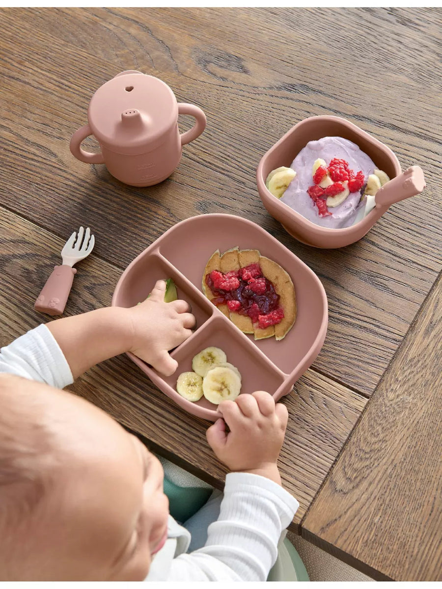 Baby weaning tray set with pink bib tray, divided plates, and spoon, on table