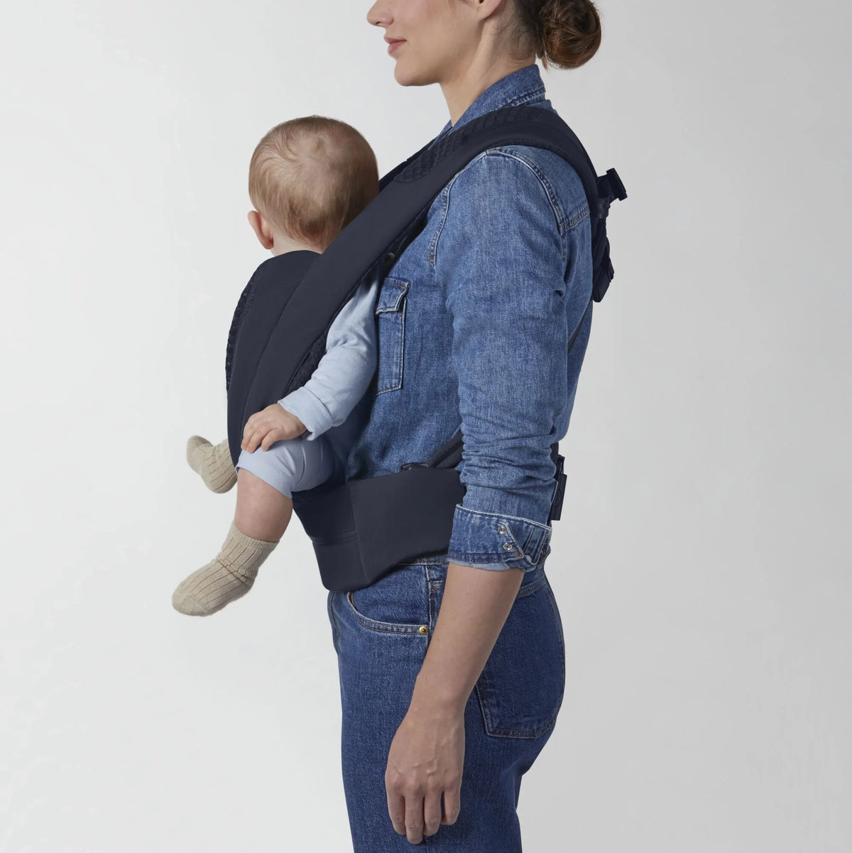 Dark blue baby carrier worn on model, rear panel and adjustable shoulder strap