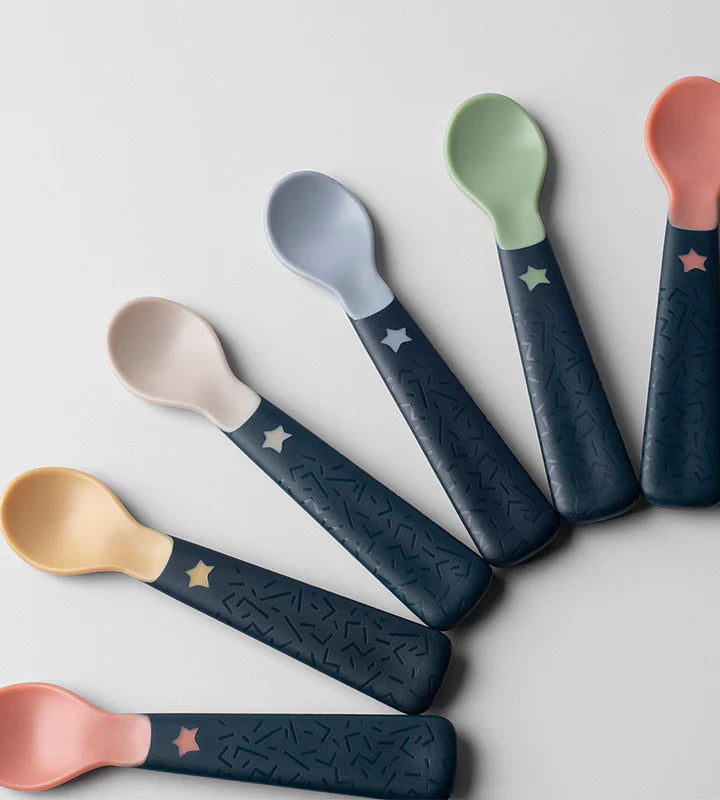 Five baby weaning spoons laid in a fan, pastel heads, dark blue star-pattern handles