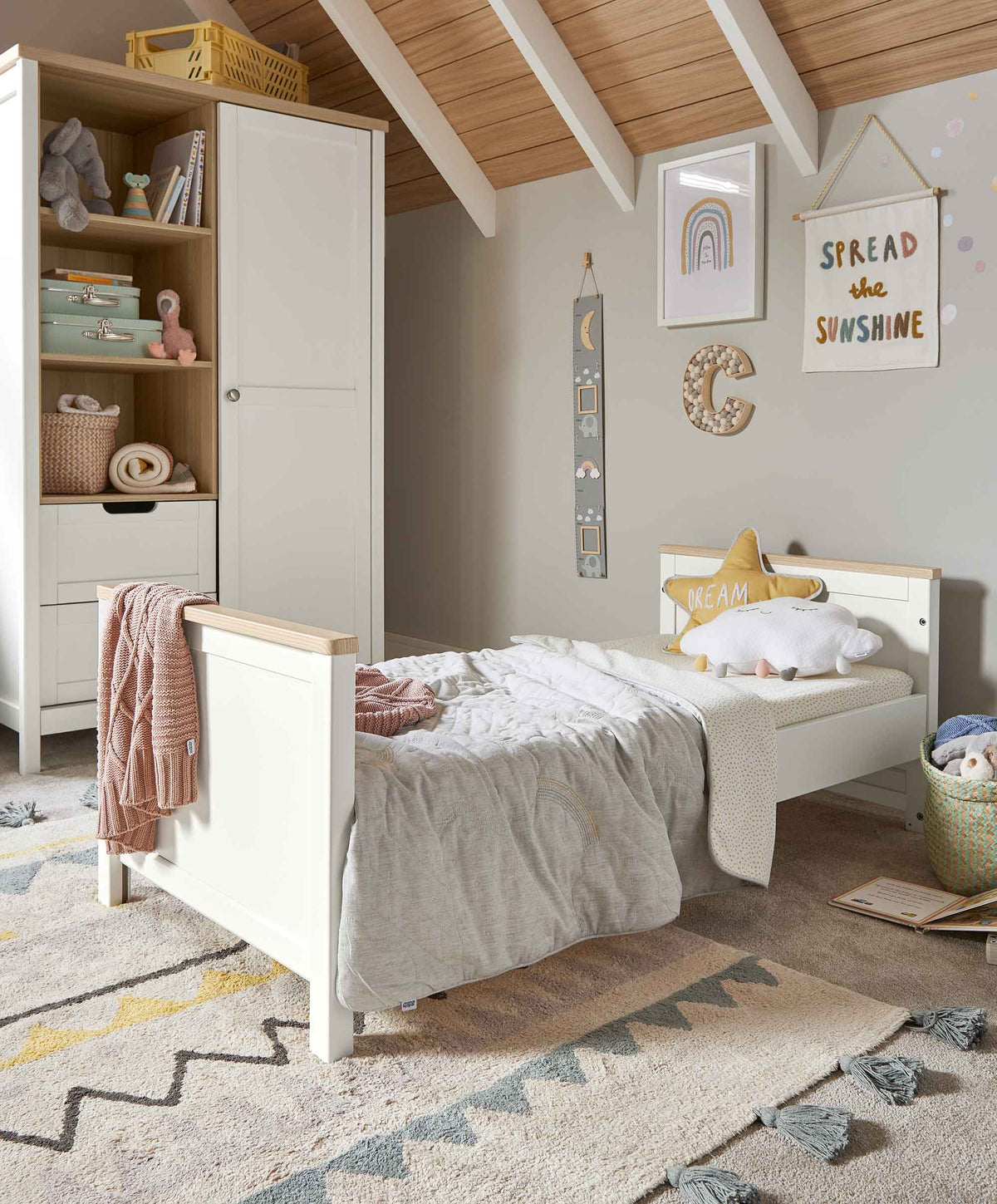 White baby cot with light wood slats and mattress, side view in a nursery