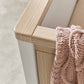 White cot corner with light wood rail and vertical slats, with a knit blanket