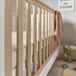 Wood and white cot end panel with vertical slats and knitted blanket on the rail