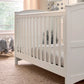 White cotbed with vertical slats and paneled side panels.