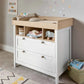 White nursery dresser changer with light wood top, open shelf, and three drawer fronts