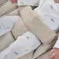 Beige bouncer harness and legrest with a white patterned baby sleeper