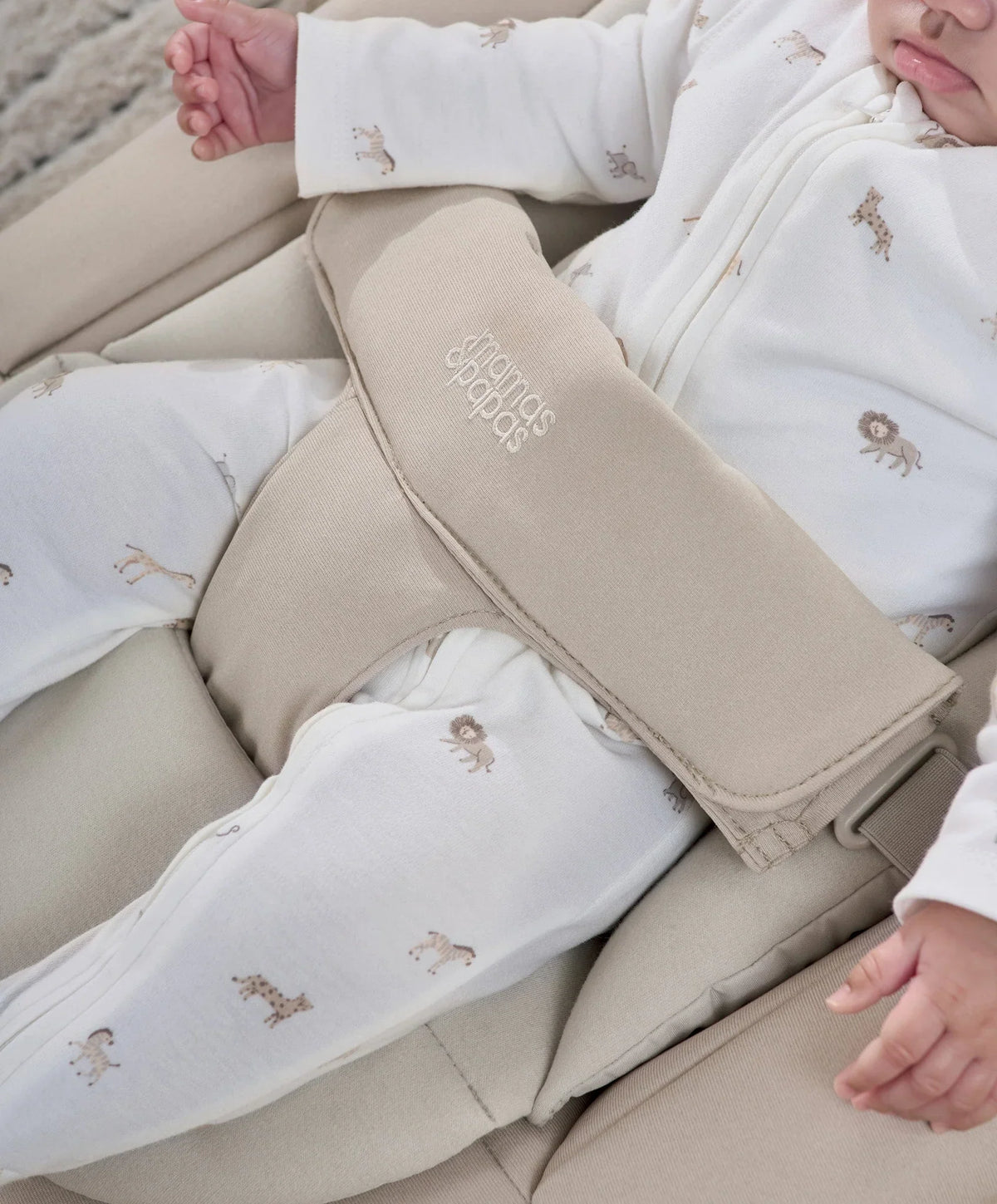 Beige bouncer harness and legrest with a white patterned baby sleeper