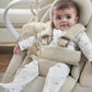 Beige baby bouncer seat with headrest, infant in a white sleeper with animal prints