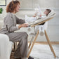 Baby bouncer with beige seat and wooden stand, infant seated
