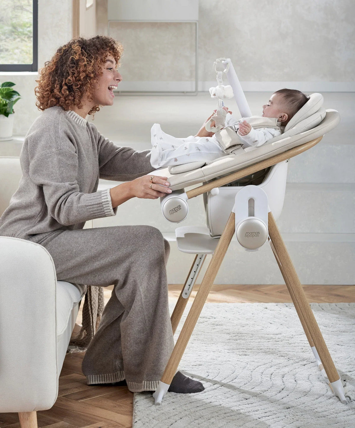 Baby bouncer with beige seat and wooden stand, infant seated