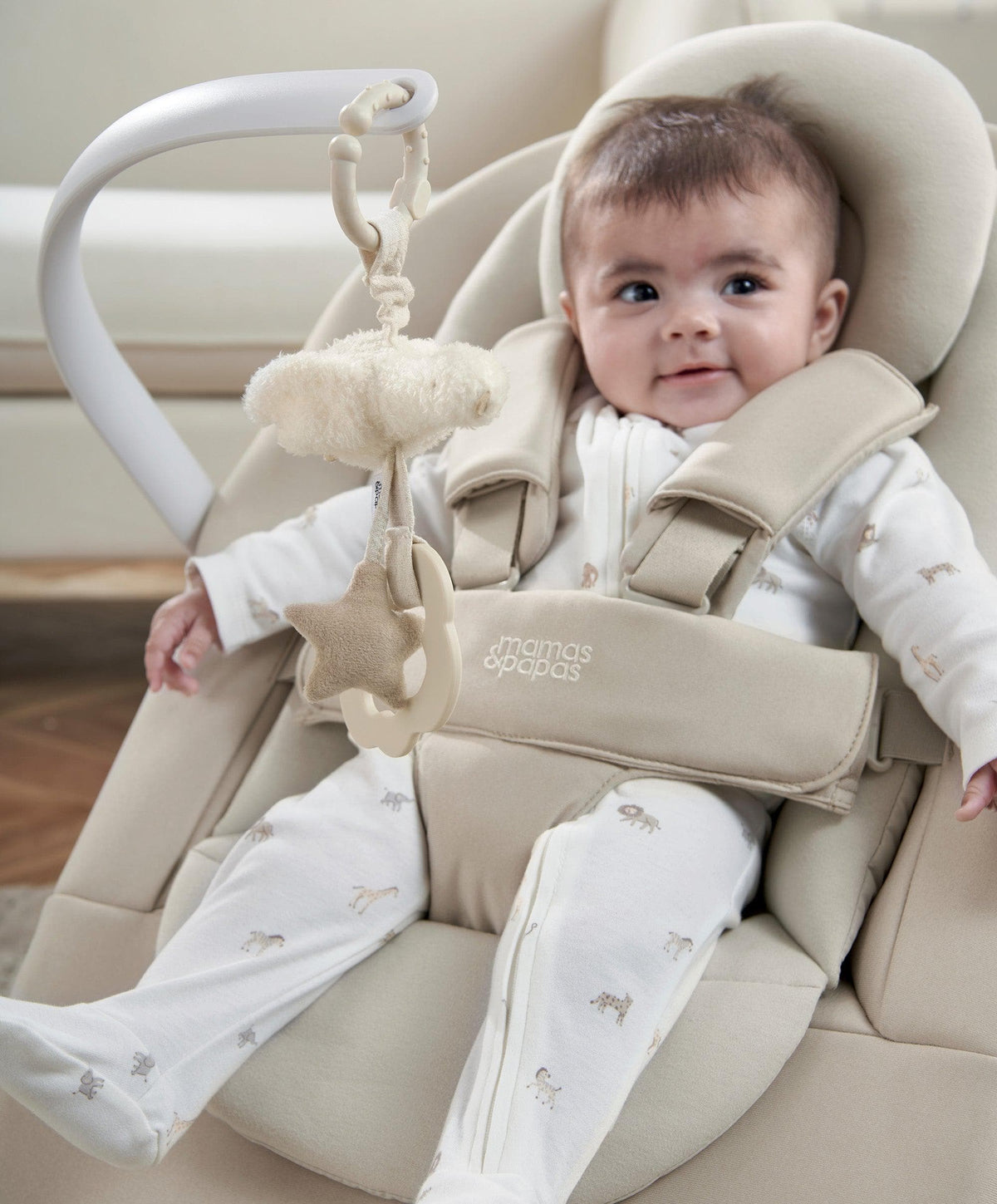 Beige baby bouncer seat in use, infant wearing white sleeper with small animal motifs