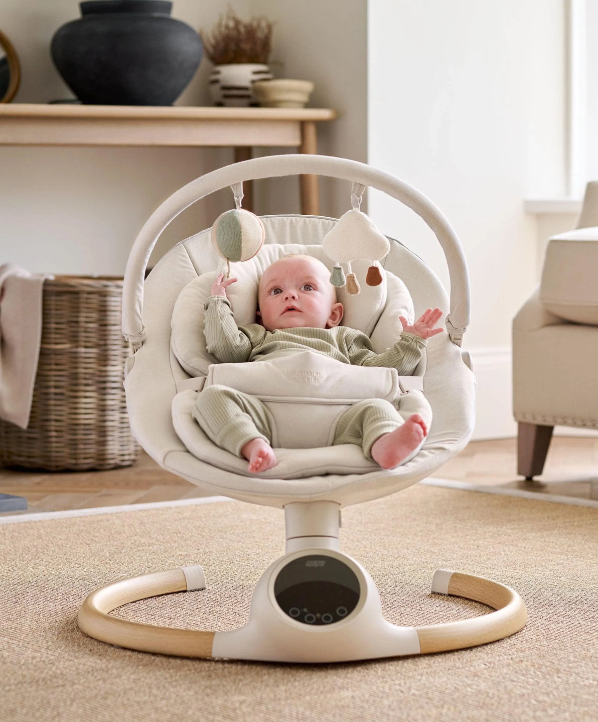 Cream baby swing with plush seat, safety harness, and hanging toy arch.