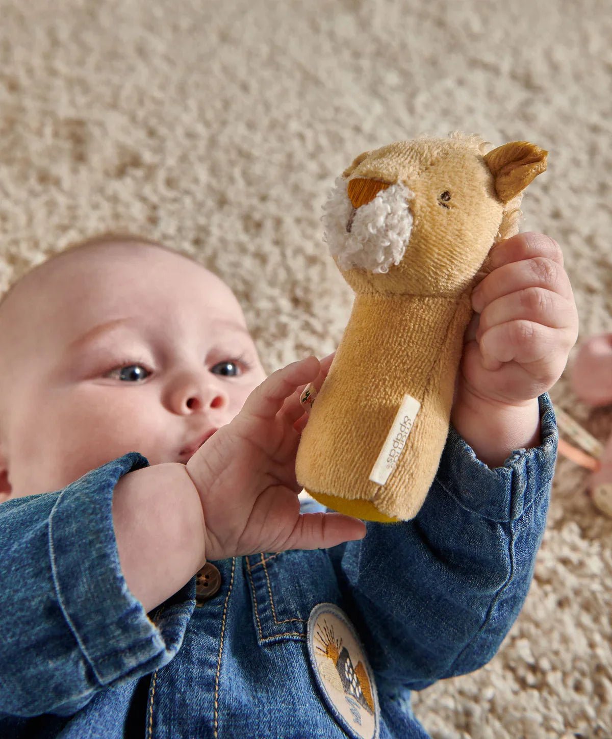 Lion mini rattle held in a hand, tan plush with white muzzle and yellow nose