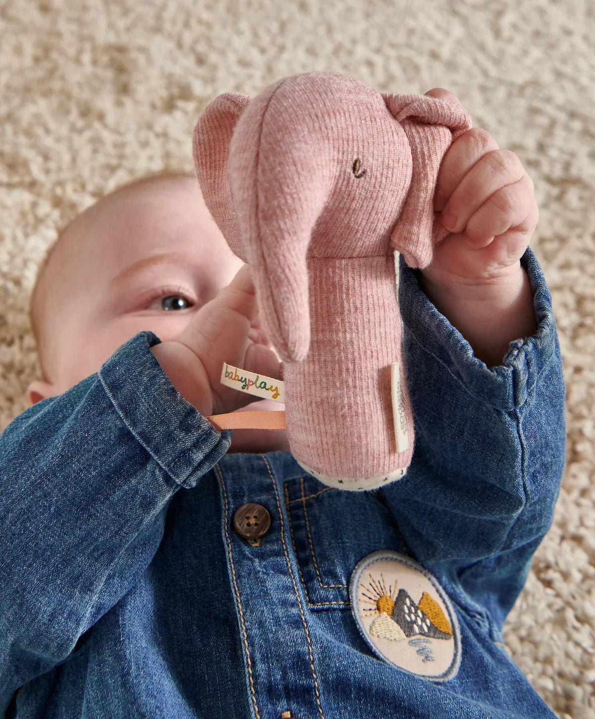 Pink elephant mini rattle held by baby hands against denim outfit