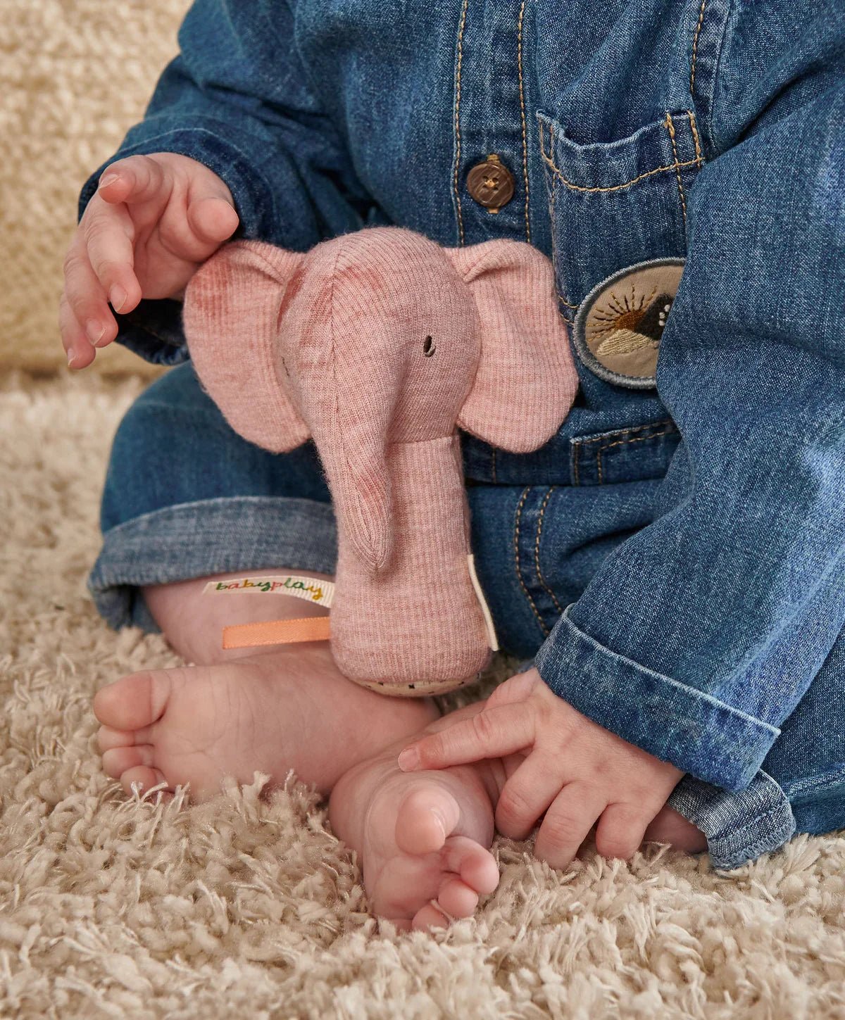 Pink elephant mini rattle with ribbon tag in baby hands over rug
