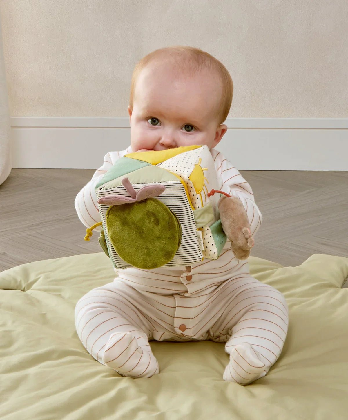 Soft activity cube with green face panel and dangling toy pieces