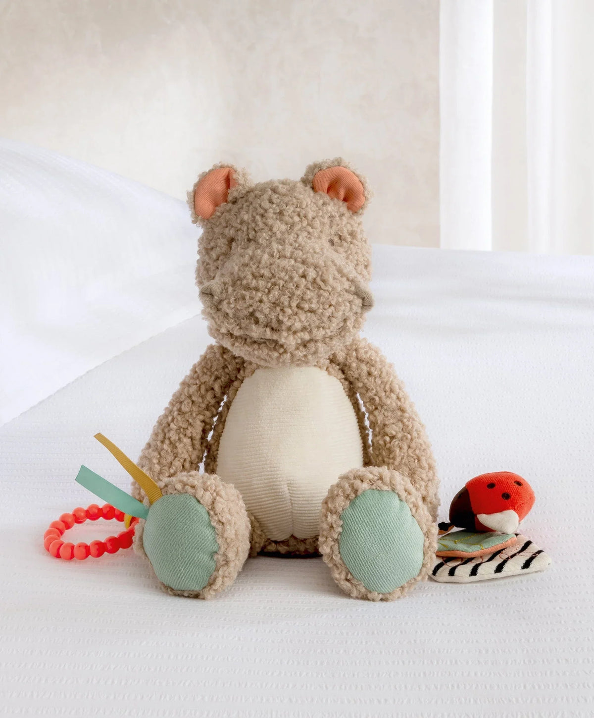 Plush activity toy hippo with textured beige body, mint feet, and dangling toys