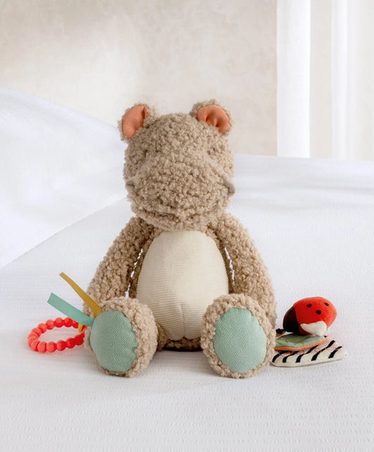 Plush activity toy hippo with textured beige body, mint feet, and dangling toys