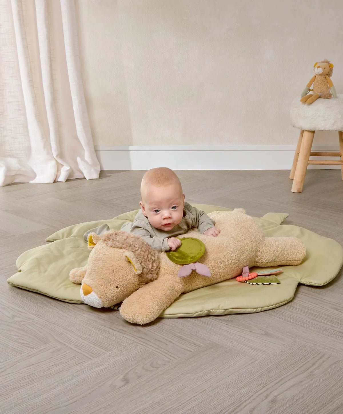 Lenny Lion tummy time plush on light green play mat, beige lion with attached teether