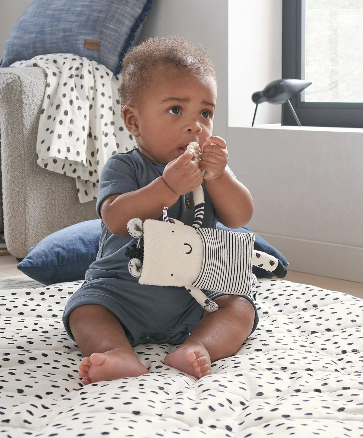 Baby holding a plush zebra activity toy with striped body and ring teether